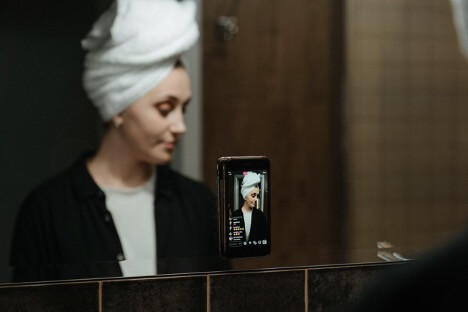 A woman in a white shirt and black jacket uses the Instagram Live feature to talk to engage with her followers.