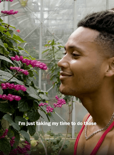 This is a screenshot of a reel where a young man is smiling and gazing at flowers. The text on the reel reads: “I’m just taking time to do those…”