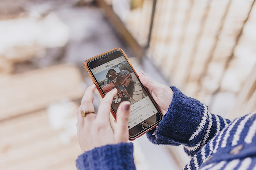 A woman with a blue sweater reading a caption on Instagram while using her iPhone.