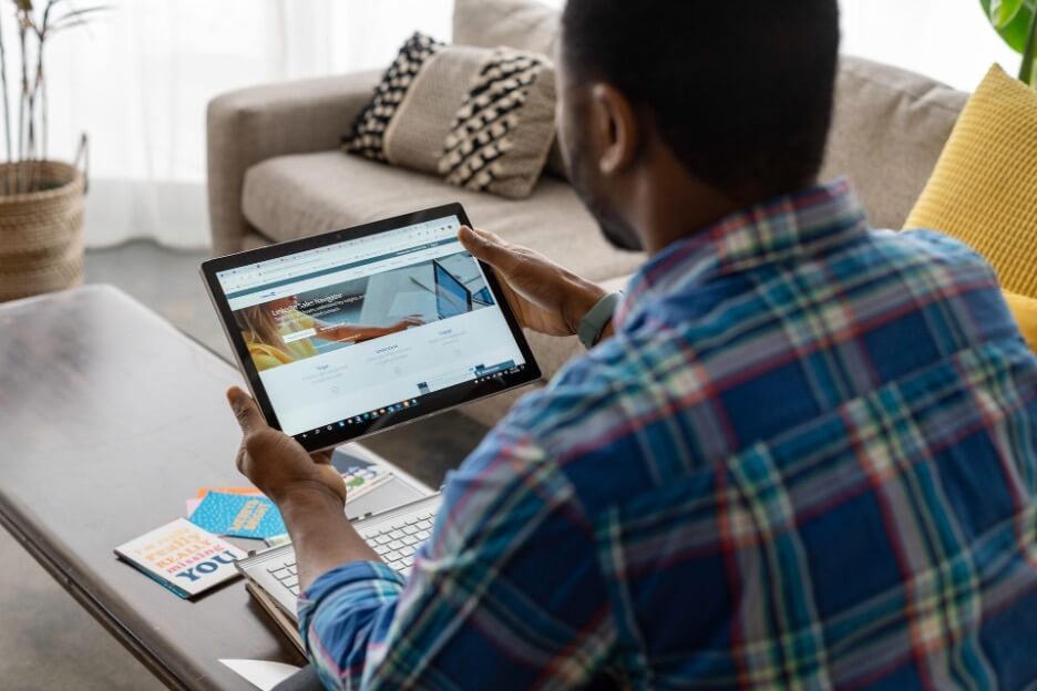 A man in a plaid shirt uses a tablet to check a LinkedIn page.