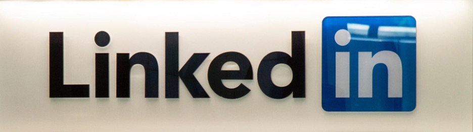 The LinkedIn logo situated on a white wall. The “Linked” letters are in black lettering. The “in” letters are in white lettering, surrounded by a blue box.