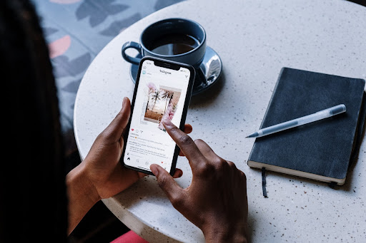 A person uses Instagram on their iPhone while drinking coffee.