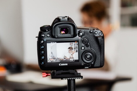 A woman films herself with a Canon DSLR camera while she works at her job.