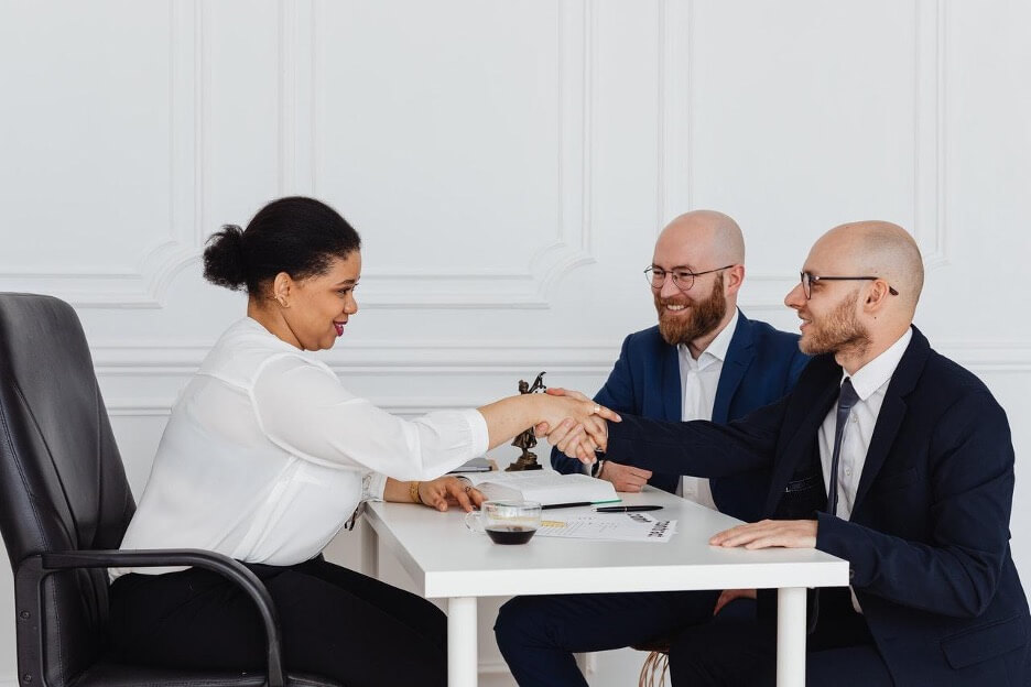 A business owner in a white blouse closes a deal with two clients in navy suits.