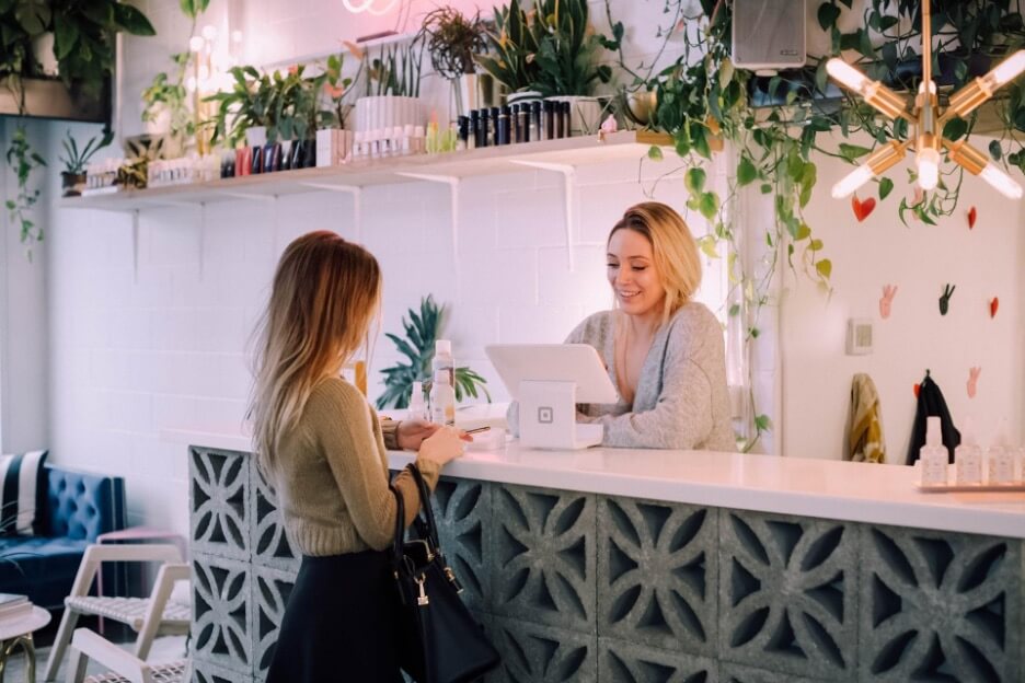 This is an image of a woman in a sage-colored sweater buying skincare products at a local shop.