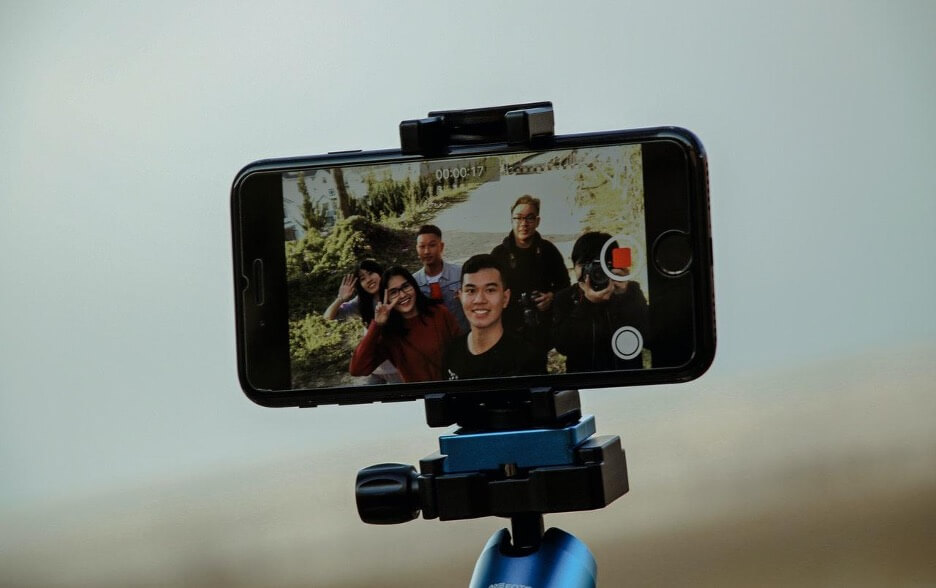 An iPhone on a selfie stick records a video of 6 people walking through a nature trail.