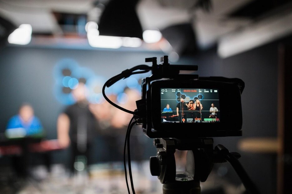 A DSLR camera records a video of a band playing a song in a studio.