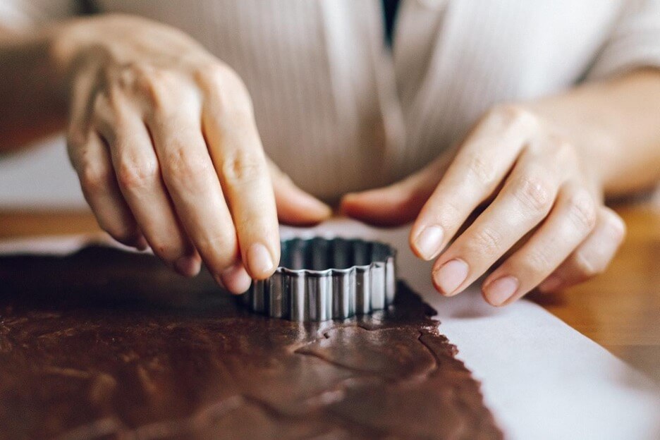 This is an image of a person using a cookie cutter to cut out shapes on chocolate-flavored dough.
