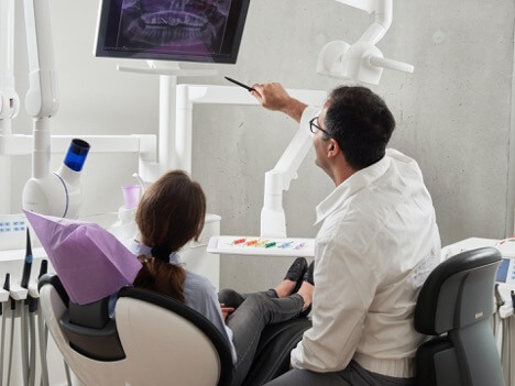 A dentist in a white jacket shows his patient an X-ray of her teeth.