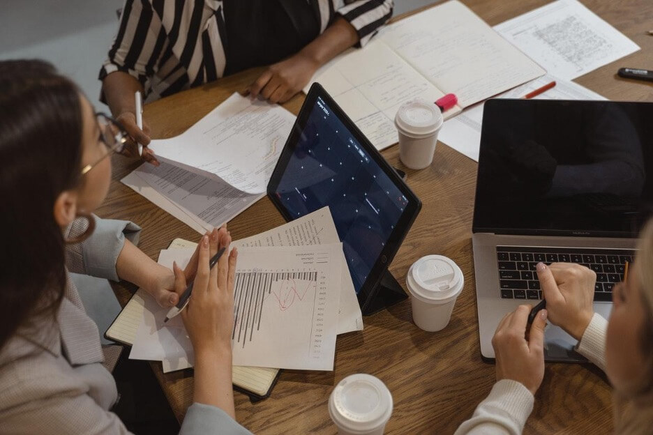 Three social media marketers discuss a new campaign for a client while one check their calendar on an iPad.