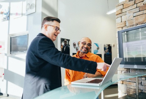 A digital marketing employee points at a laptop to show a client where they could improve their business.