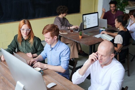 A group of employees at two different tables meet to discuss the marketing plans for their clients.