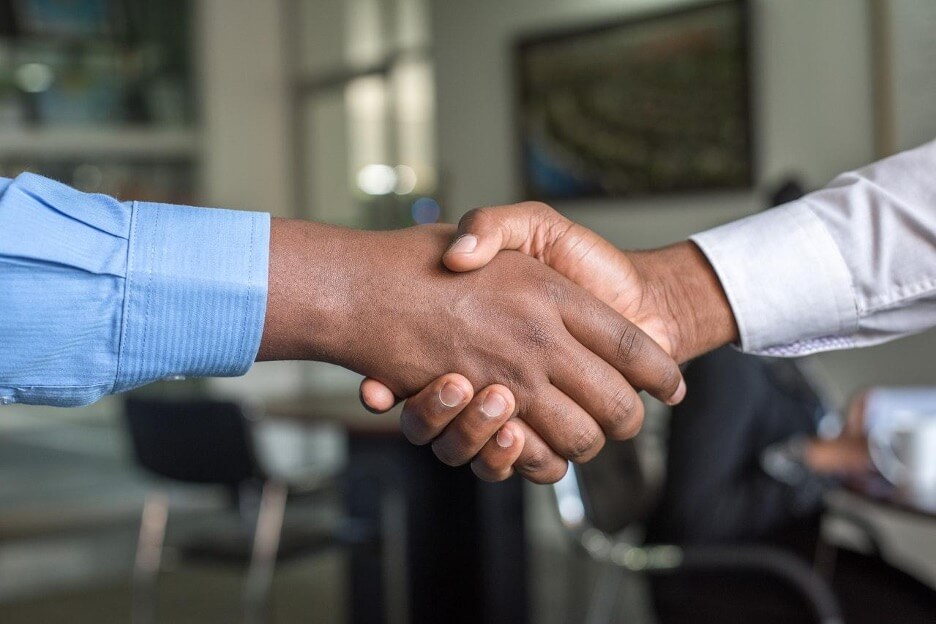 A man in a blue pin-stripe shirt shakes hands with another man wearing a white shirt.