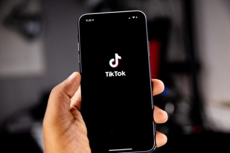 A person holds an iPhone with the TikTok logo displayed on the screen.