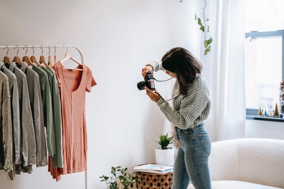 A woman in a gray sweater takes pictures of an orange shirt with a DSLR camera.
