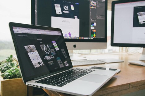 This is an image of a wooden desk with two monitors and a laptop all displaying a design for a client.