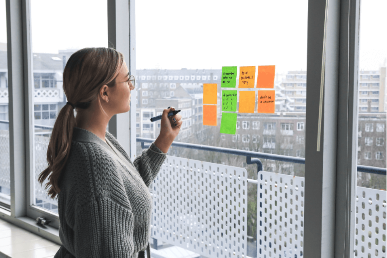 A manager at a marketing agency is planning a strategy for a client as she writes on a series of post-its that are stuck to a window.