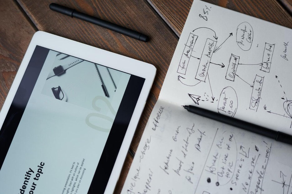 This is an image of an android tablet next to a notebook with a marketing strategy written in it.