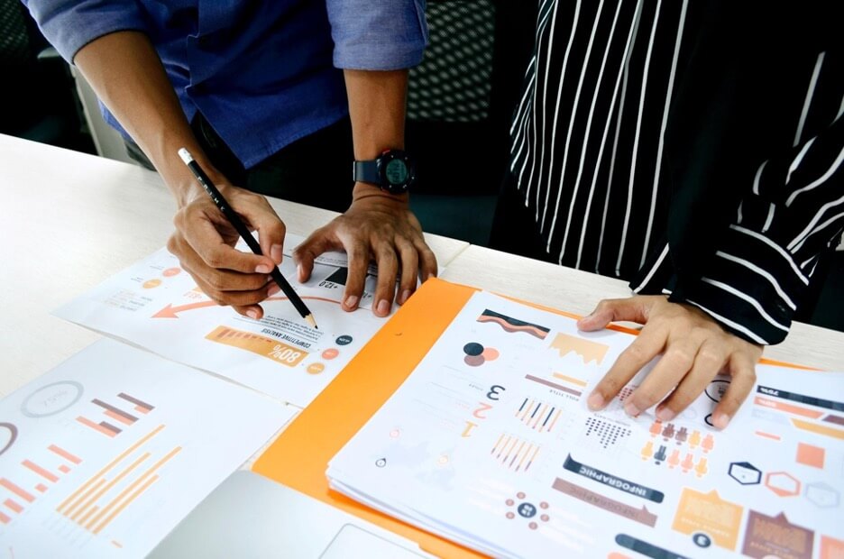 Two marketing managers discuss the analytics of a client’s social media account over a white tabletop.