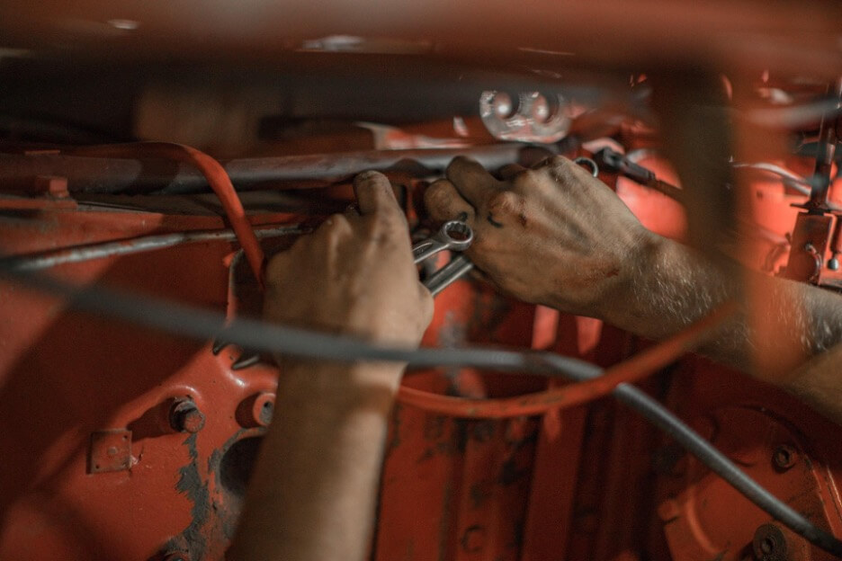 This is an image of a mechanic with a wrench in their left hand as they adjust some cables inside a red vehicle.