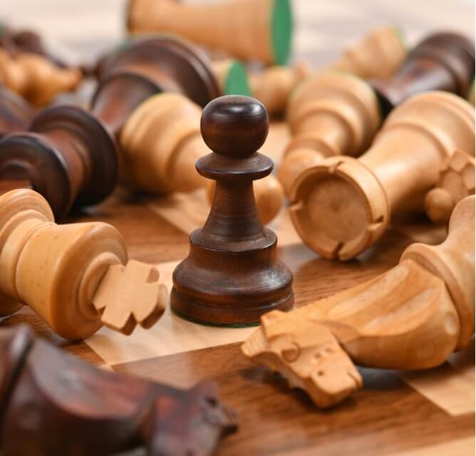 A pawn standing on a chessboard around different chess pieces that have been knocked down.