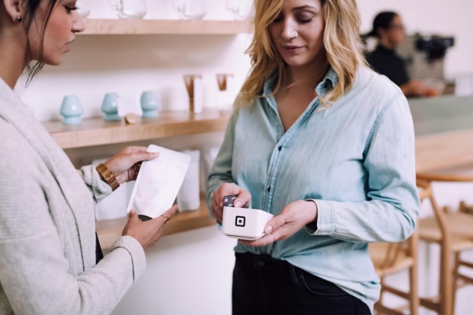 A woman with a light blue denim shirt pays for her bill at a coffee shop.