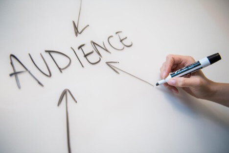 A person’s hand writes “Audience” on a whiteboard with a black marker.