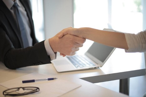 Two people sit around a table and shake hands after agreeing on a business plan.