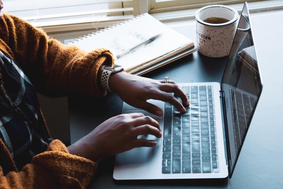 This is an image of a social media marketer writes an article on a Macbook while they drink coffee.