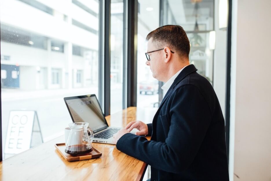 A social media marketer uses his laptop to check a business account on LinkedIn while he drinks coffee.