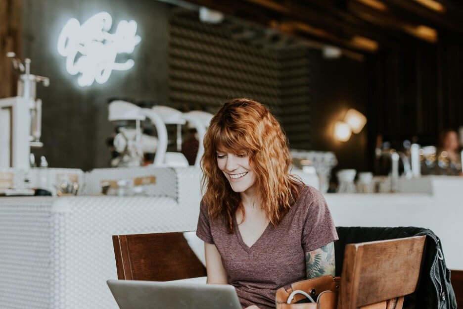 A woman sits at a cafe while she reads a new article published on LinkedIn.