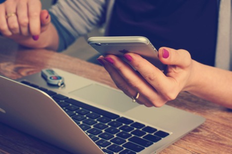 A social media manager uses her iPhone to read comments, while she uses her MacBook to create more content for social media.