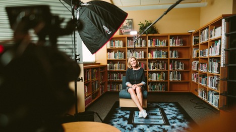 A  woman in a black dress smiles as she waits for her moment to talk in front ot the camera.