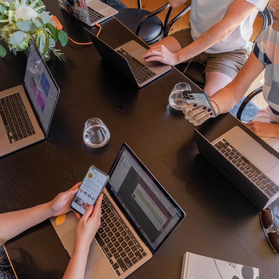 Three digital marketers work on a strategy for a client while they sit around a dark brown desk.