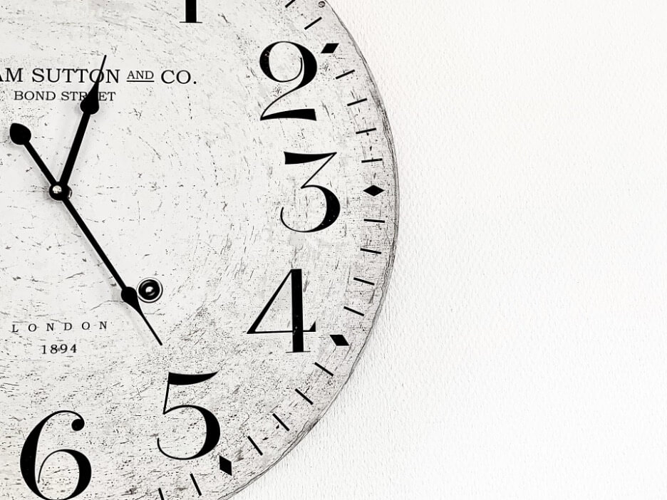 A vintage white face clock with black hands shows that the time is: “1:25.”