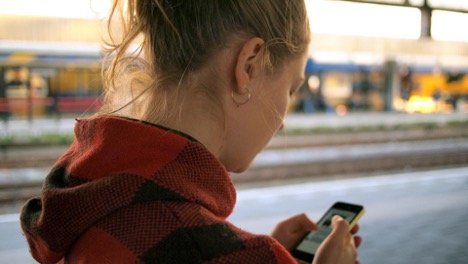 A woman wearing a red jacket uses her yellow iPhone to check her social media.