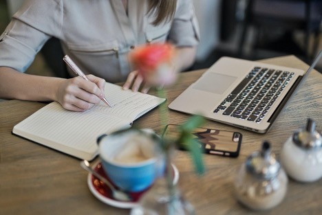  A woman looks at her MacBook while taking notes of what a competitor is doing on social media.