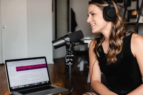 A woman records herself while sitting in front of a black microphone. She smiles and directs her attention to the camera.