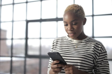 A woman with blonde hair and a striped long-sleeved t-shirt scrolls through social media with her iPhone.