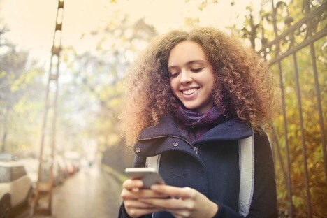  A woman in a navy coat smiles while she looks at her gray iPhone.