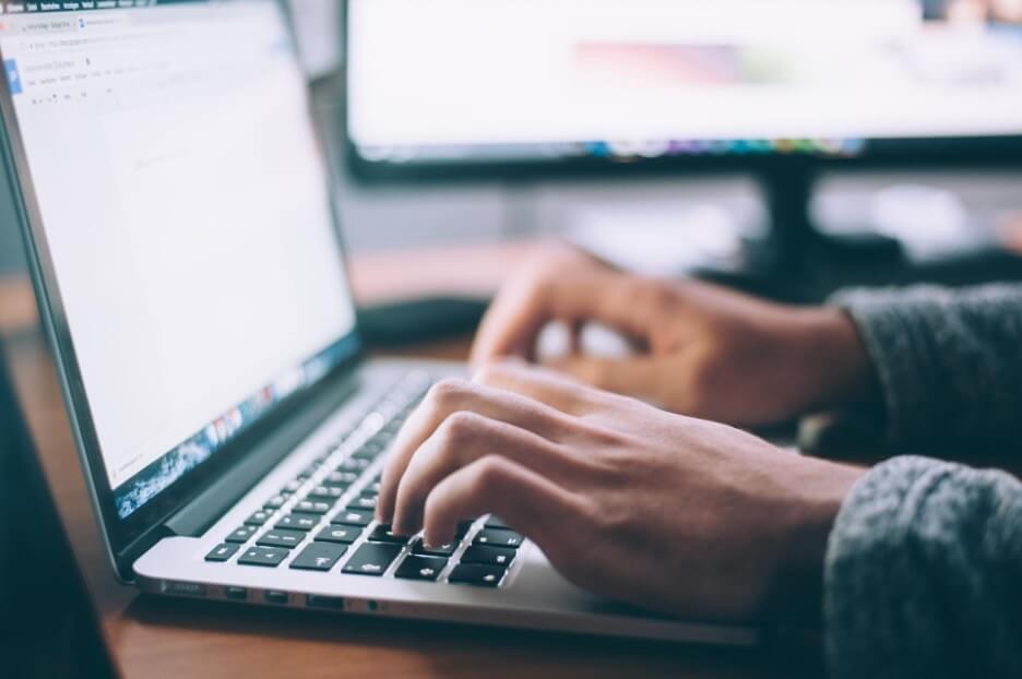 A person uses a Macbook Pro to write an article on Google Docs.