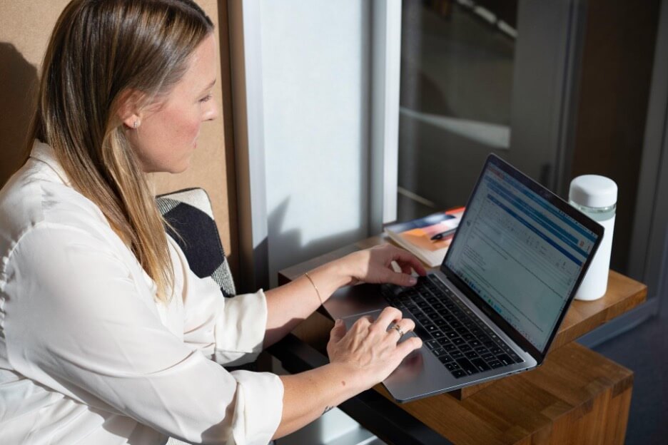 A woman in a white shirt writes an article on her Macbook Pro.