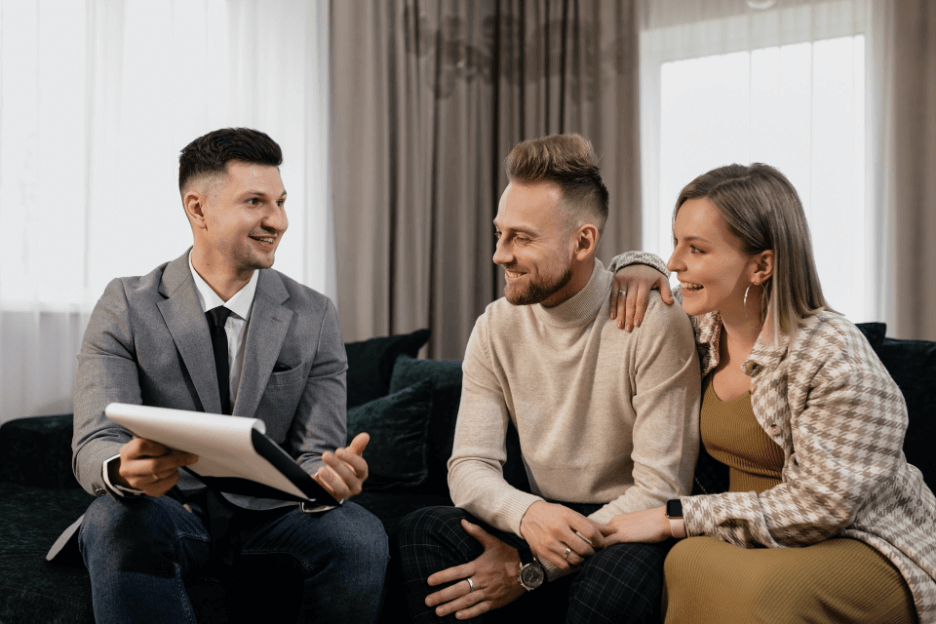 A young couple smiles as they listen to the businessman explain the services he provides. He smiles, too.