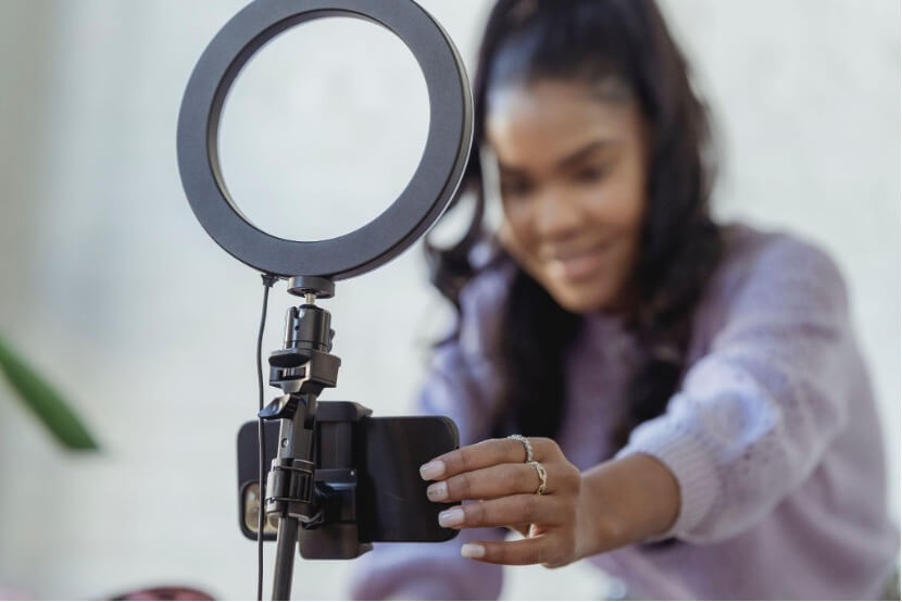 An influencer in a lavender-colored blouse is tilting her smartphone as she gets ready to film