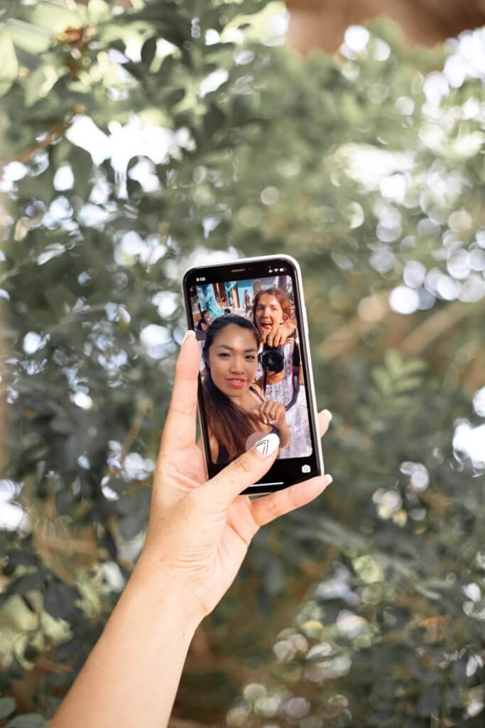 A woman taking a photo on her iPhone with her friend behind her.